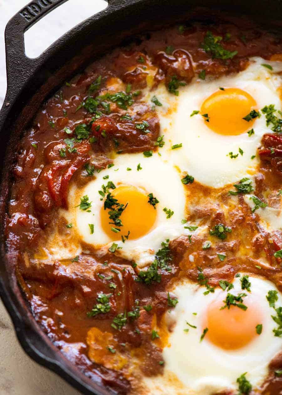 关闭在一个黑煎锅的Shakshuka中东被烘烤的鸡蛋，新鲜的炉子