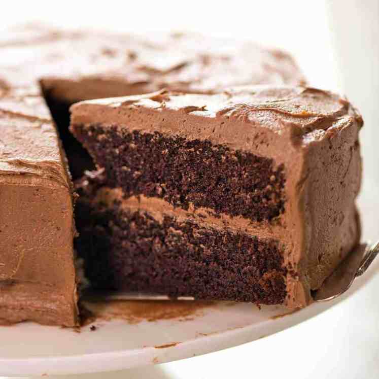 一张照片显示，在白色蛋糕架上，有半块巧克力蛋糕上涂着奶油巧克力，有一大块蛋糕被拉了出来。