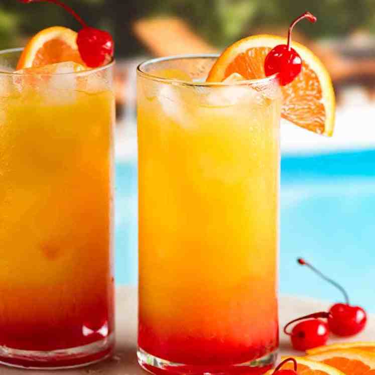 两杯龙舌兰日出鸡尾酒在泳池边，配以橙子片和酒浸樱桃准备饮用